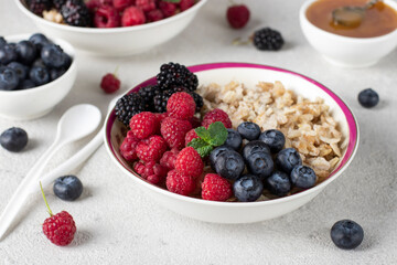 Oatmeal porridge with blueberries, raspberry, blackberry and honey on light gray background. Breakfast meal concept
