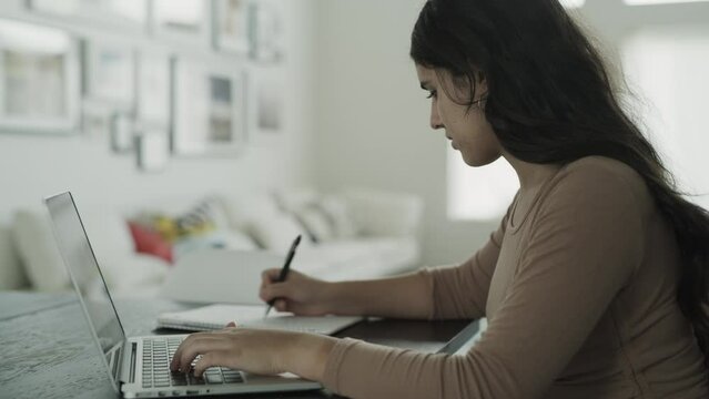 Close up of teenage girl using laptop for online school and taking notes / Lehi, Utah, United States