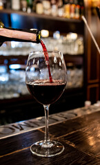 bartender pouring red wine into a glass in cafe or bar on the bar counter