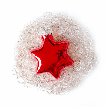 Red glass star, bedded in a silvery-white angel hair nest, over a white background. A star shaped Glass bauble, to hang on a Christmas tree, on a metallic tinsel pad. Decorative Christmas ornament.