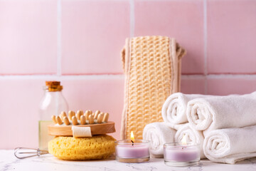 Fototapeta na wymiar Spa setting with burning candles, towels, wisk, massager against pink tiled wall. Beauty blogging, salon care concept. Selective focus. Place for text.
