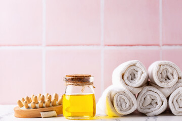 Spa setting with  bottle with oil, towels  and massager against pink tiled wall.   Beauty blogging, salon  care concept. Selective focus. Place for text. - 551079711