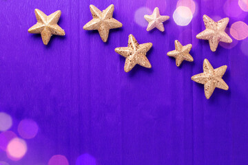 Postcard with big and small golden decorative stars and bokeh light on violet  paper textured background. Top view. Christmas, New Year holidays concept.  Place for text.