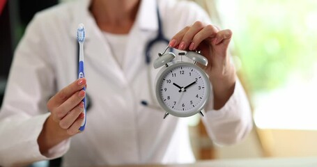 Doctor dentist showing alarm clock and toothbrush in clinic closeup 4k movie slow motion