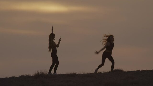 Silhouette of woman recording friend dancing at sunset / Cisco, Utah, United States