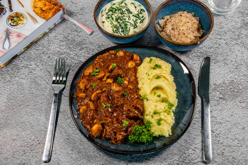 goulash with mushrooms served with masched potatoes, cabbage and spinach in sour cream on blue tableware