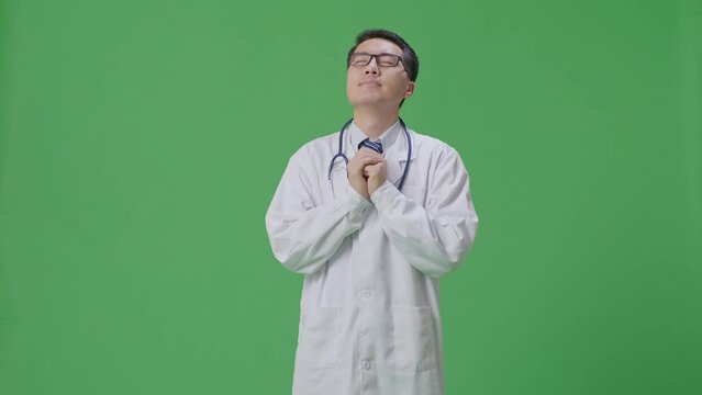 Asian Male Doctor With Stethoscope Pray For Something On Green Screen Background In The Hospital
