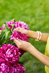 Little girl in the garden in bushes of peonies, child touch the flower