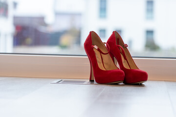 Red high heel pumps in front of a window and on a light floor