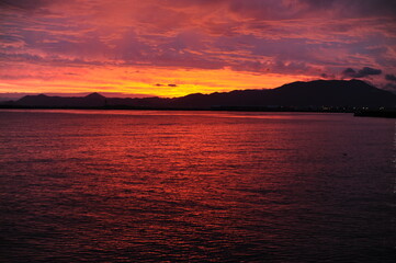 Red, pink, orange and violet sunrise at the seaside during dawn with clouds in the sky and mountains on the shore of a port
