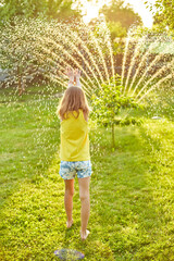 Happy kid girl playing with garden sprinkler run and jump, summer