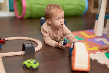 Adorable toddler playing with car toy lying on floor at kindergarten