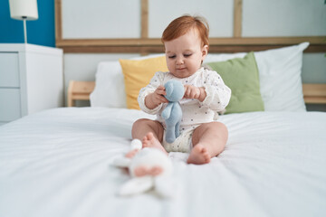 Adorable redhead toddler playing with doll sitting on bed at bedroom