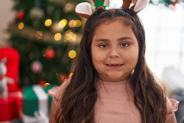 Plus size hispanic girl wearing reindeer ears standing by christmas tree at home