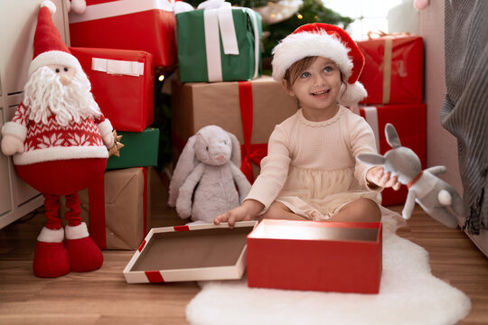 Adorable girl unpacking gift sitting by christmas tree at home