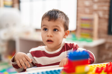 Adorable toddler playing with construction blocks sitting on table at kindergarten