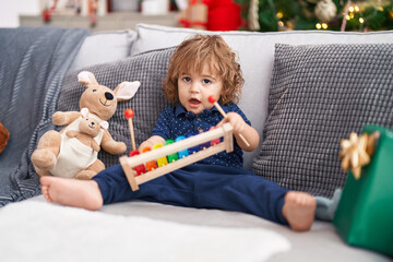 Adorable hispanic toddler playing xylophone sitting on sofa by christmas gifts at home