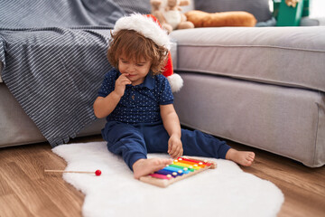 Adorable hispanic toddler wearing christmas hat playing xylophone at home