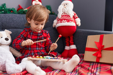 Adorable hispanic girl playing xylophone sitting on sofa by christmas decor at home