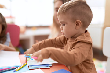 Adorable toddler student drawing on notebook sitting on table at kindergarten