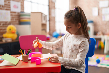 Adorable hispanic girl playing with toys sitting on table at kindergarten