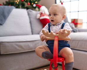 Adorable caucasian baby playing with reindeer rocking by christmas tree at home