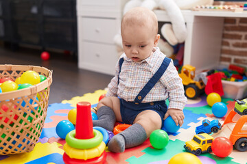 Adorable caucasian baby playing with balls sitting on floor at kindergarten