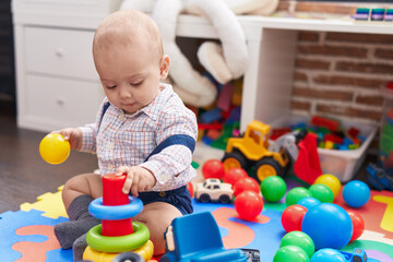 Adorable caucasian baby playing with balls and hoops sitting on floor at kindergarten