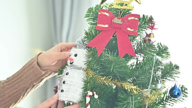 Woman hands hanging a snowman on decorated Christmas tree during Christmas festival and New Year celebration.