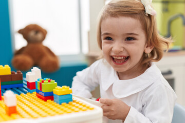 Obraz na płótnie Canvas Adorable caucasian girl playing with construction blocks sitting on table at kindergarten