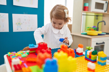 Adorable caucasian girl playing with construction blocks standing at kindergarten