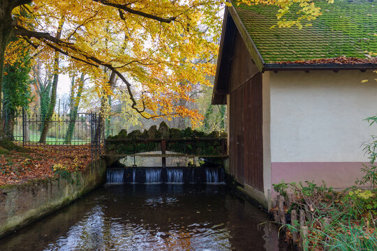 Historische Brücke mit kleiner Staustufe im Englischen Garten in Freiburg Hugstetten. Herbstliche Farben an den Blättern der Bäume.