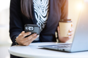 Close-up shot of young woman using smartphone and laptop computer sitting in cafe