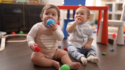Two toddlers sucking ball sitting on floor at kindergarten