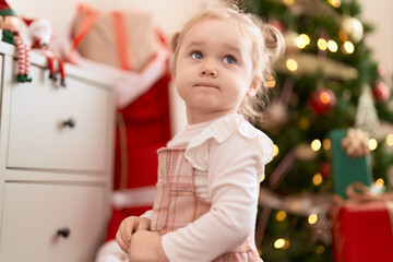 Adorable caucasian girl standing by christmas tree at home