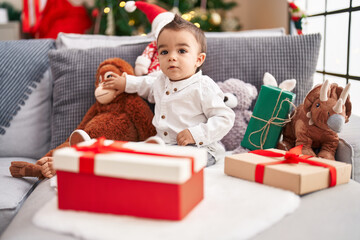 Fototapeta na wymiar Adorable hispanic toddler sitting on sofa by christmas tree at home