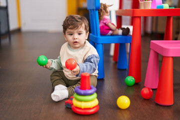 Adorable hispanic toddler playing with balls sitting on floor at kindergarten