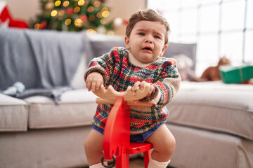 Adorable hispanic toddler crying and playing with reindeer rocking by christmas tree at home