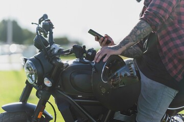 Tattooed Caucasian man wearing a red plaid shirt looking at his phone while on a motorcycle