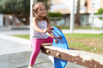 Adorable hispanic girl sitting on swing playing at park playground