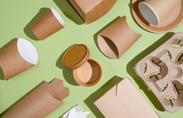 A lot of paper disposable tableware is stacked evenly on a green background. Use of eco-friendly...