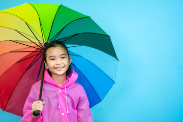 Children close up photo of cute and cheerful people, holding umbrella and wearing rain coat looking and smile on blue pastel background