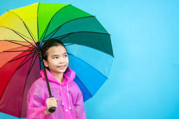 Children close up photo of cute and cheerful people, holding umbrella and wearing rain coat looking and smile on blue pastel background