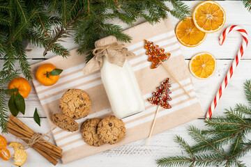 milk and cookies on the table with spruce branches, christmas treats for Santa Claus, tangerines, cinnamon, christmas traditions, flat lay