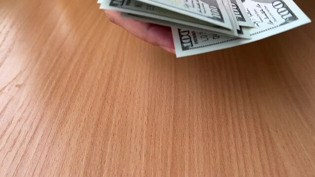 Female hands count paper American green banknotes of 100 USD on background of wooden table. One hundred dollars USA. Concept of accounting, immigration, getting paid, travel, tourism. Salary. Bill