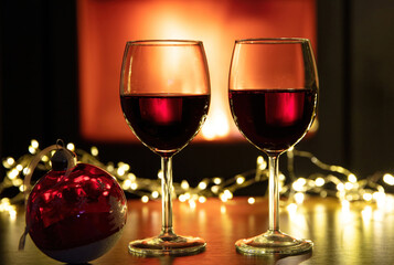 Christmas celebration. Red wine glasses and decoration on table, fireplace background. Xmas celebration