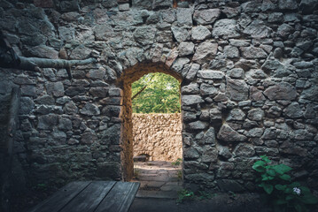A doorway in the wall of a ruined castle through which sunlight spills.