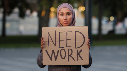 Sad muslim woman in hijab standing outdoors islamic ethnic girl upset unemployed worry stressful lady poor female showing holding cardboard banner sign need work, dismissal pandemic covid crisis
