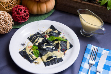 Black ravioli with cheese sauce, mixed peppers and basil leaves