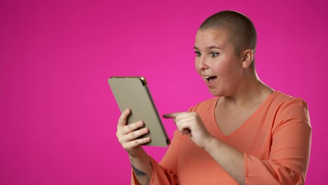 Portrait of happy smiling gender fluid non binary woman promoter 20s shopping online on mobile tablet computer giving thumbs up isolated on pink background studio with copy space